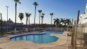 A swimming pool with a curved design, surrounded by palm trees and a fence. - Casa Caracol, Apartamento Totalmente Equipado Para su Estancia en San Carlos Son (San Carlos Guaymas)