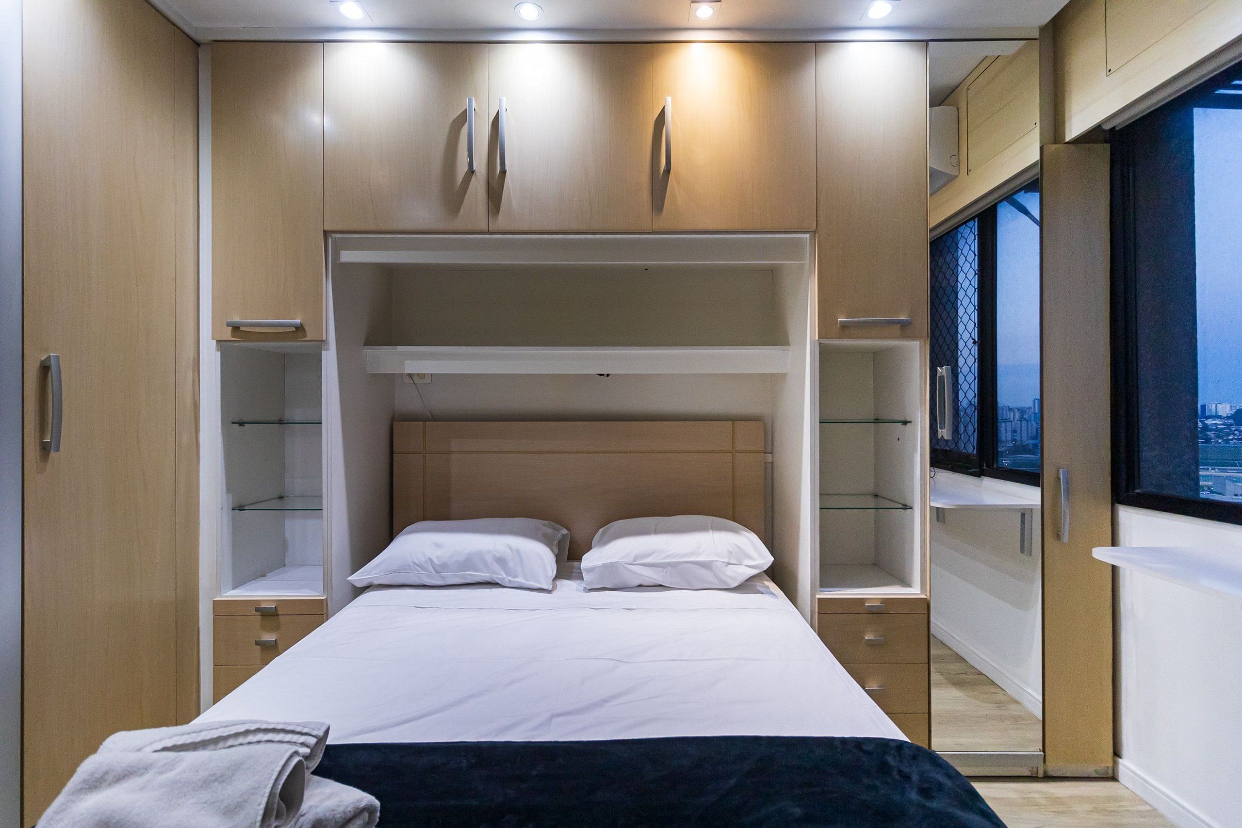 Una camera da letto con un letto a castello, scaffali a muro e un'ampia finestra vista città.