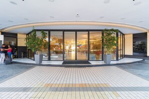 A modern building entrance with glass doors, potted plants, and a tiled floor.