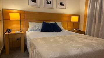 Quarto de hotel com uma cama grande, duas mesas de cabeceira, um criado-mudo e três quadros na parede.