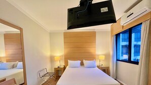 Ein Hotelzimmer mit einem großen Bett, zwei Nachttischen mit Lampen, einem Sessel, einem Spiegel und einem Fenster mit Vorhängen.