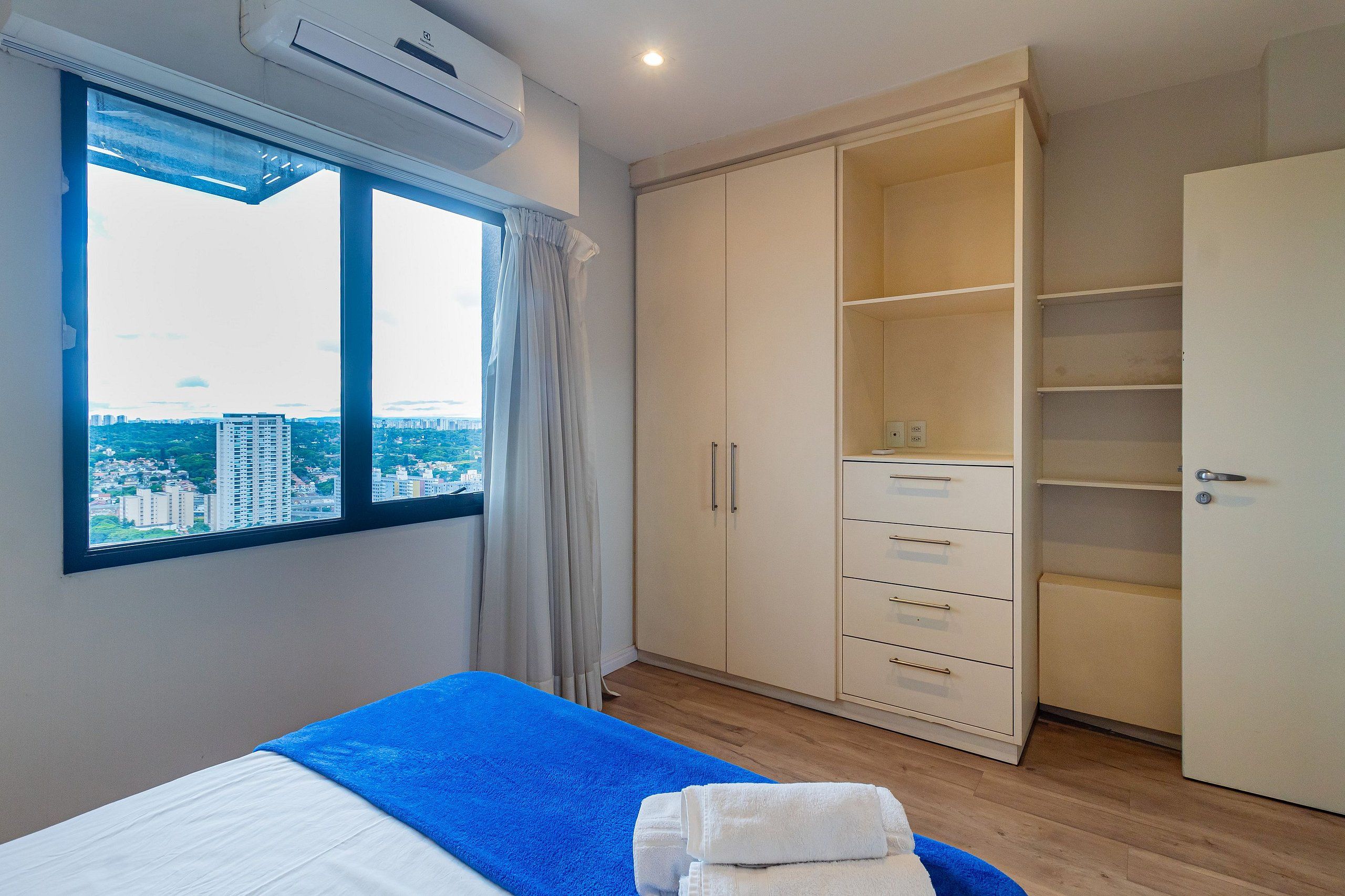 A bedroom with a bed, a wardrobe, and a window with a city view.