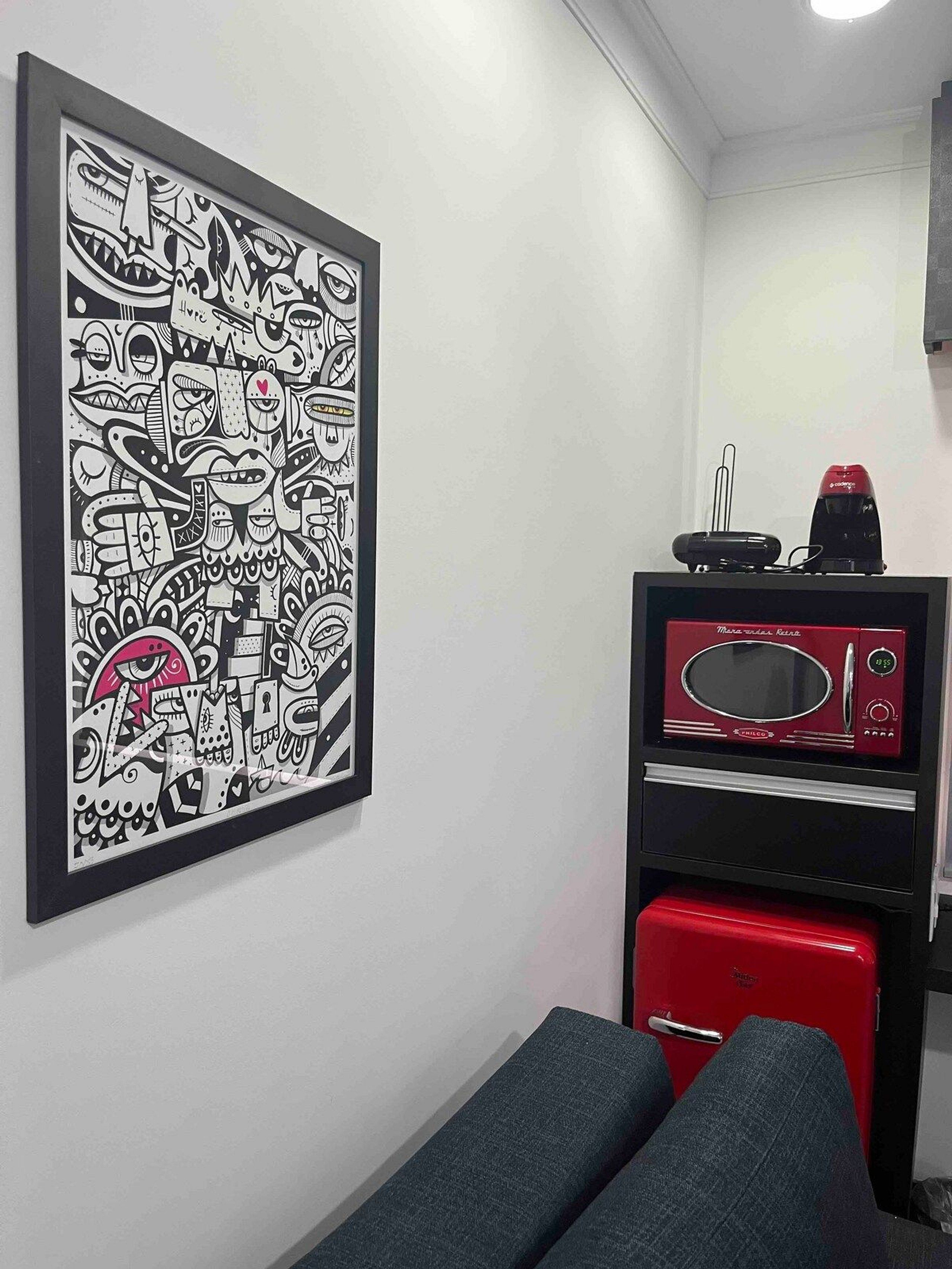 Una habitación con un cuadro abstracto en blanco y negro en la pared, un microondas rojo y un electrodoméstico rojo debajo.