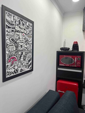 Una habitación con un cuadro abstracto en blanco y negro en la pared, un microondas rojo y un electrodoméstico rojo debajo.
