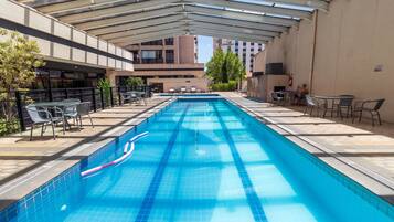 Uma piscina com teto de vidro, rodeada por espreguiçadeiras e mesas.