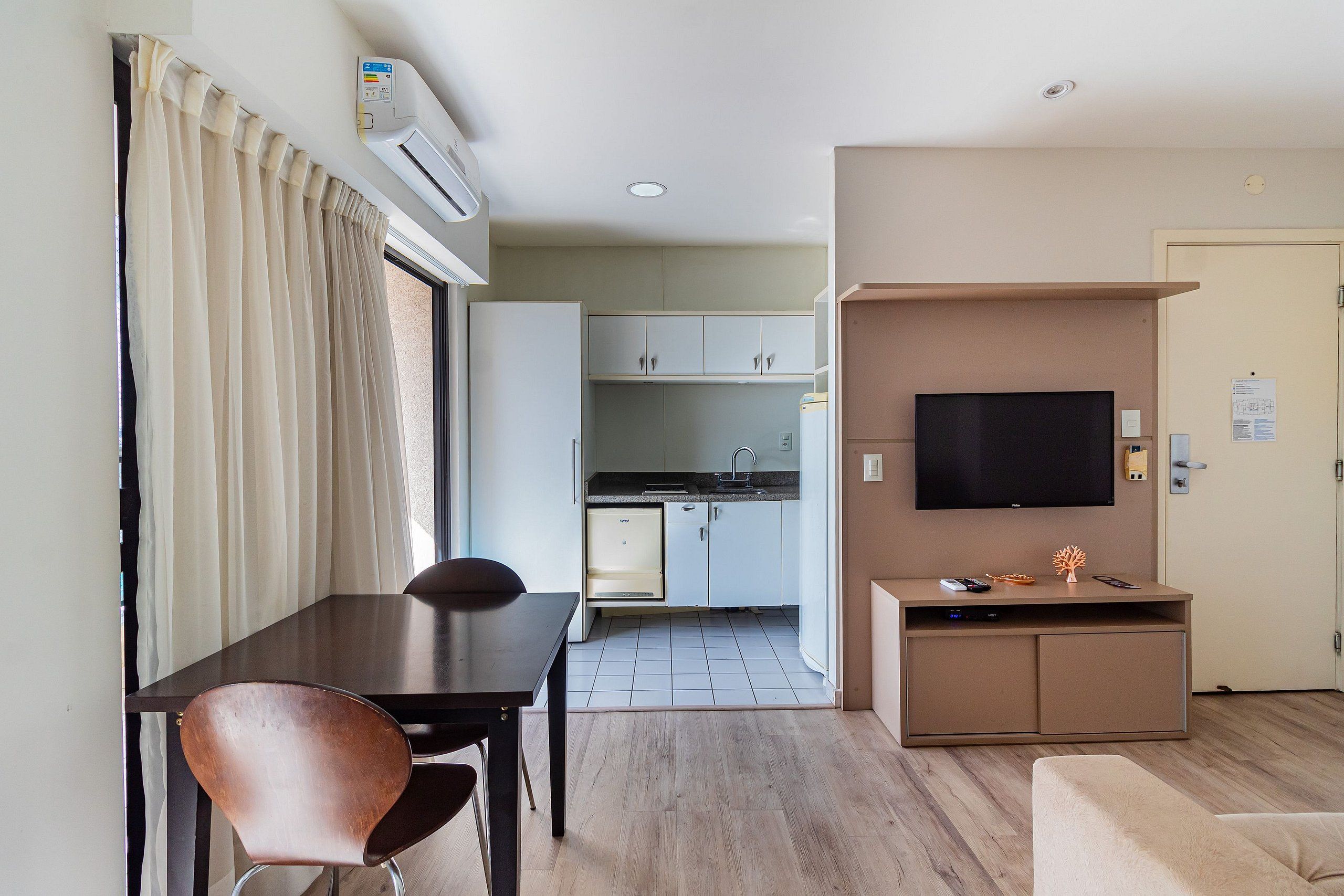 A compact living space with a dining area, kitchenette, and a TV mounted on a cabinet.
