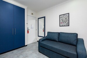 Una habitación con un armario azul, un sofá gris y una obra de arte abstracta enmarcada en la pared.