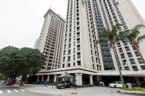 Un immeuble de grande hauteur, avec de nombreux étages, un hall d’entrée abrité et quelques voitures garées.