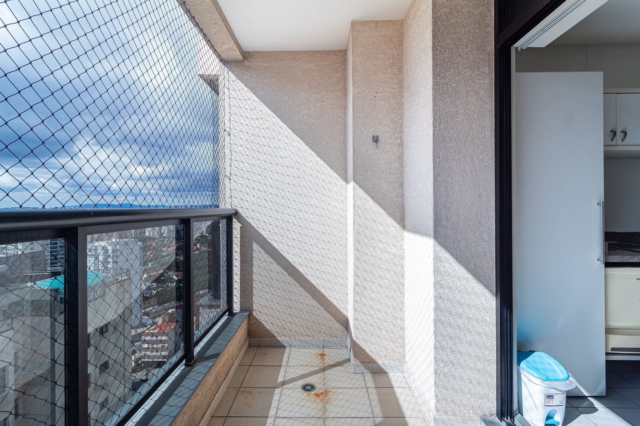 A balcony with a chain-link fence, a tiled floor, and a trash bin.