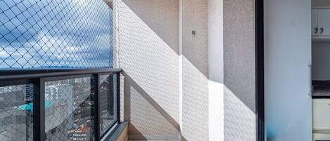 A balcony with a chain-link fence, a tiled floor, and a trash bin.