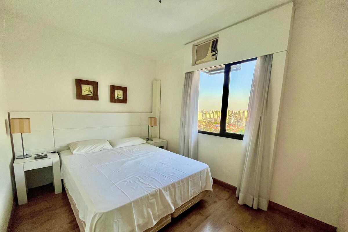 Ein Hotelzimmer mit einem großen Bett, zwei Nachttischen mit Lampen, einem Fenster mit Vorhängen und Blick auf die Stadt.