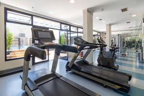 Une salle de sport équipée de tapis de course, d’une machine de musculation et d’un écran numérique.