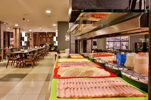 Ein reichhaltiges Buffet mit verschiedenen Speisen und eine Sitzgelegenheit mit Tischen und Stühlen.