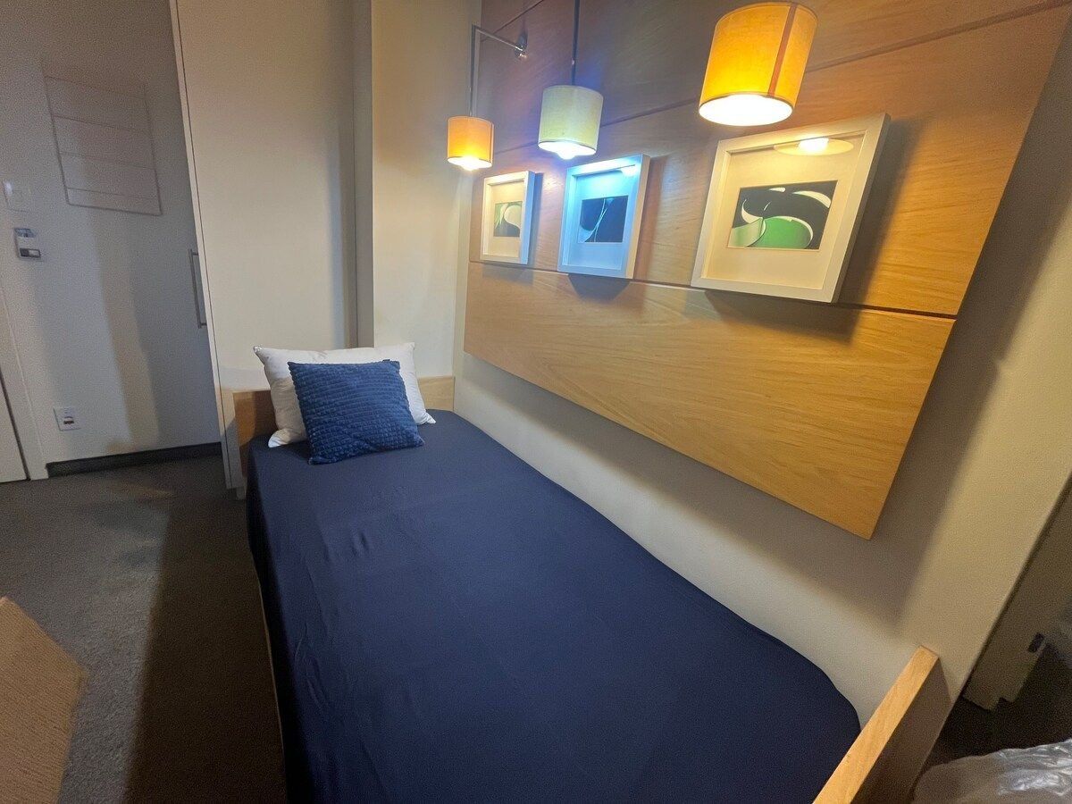 Een eenpersoonsbed met een blauwe matras en kussens, een houten hoofdbord en drie wandlampen.
