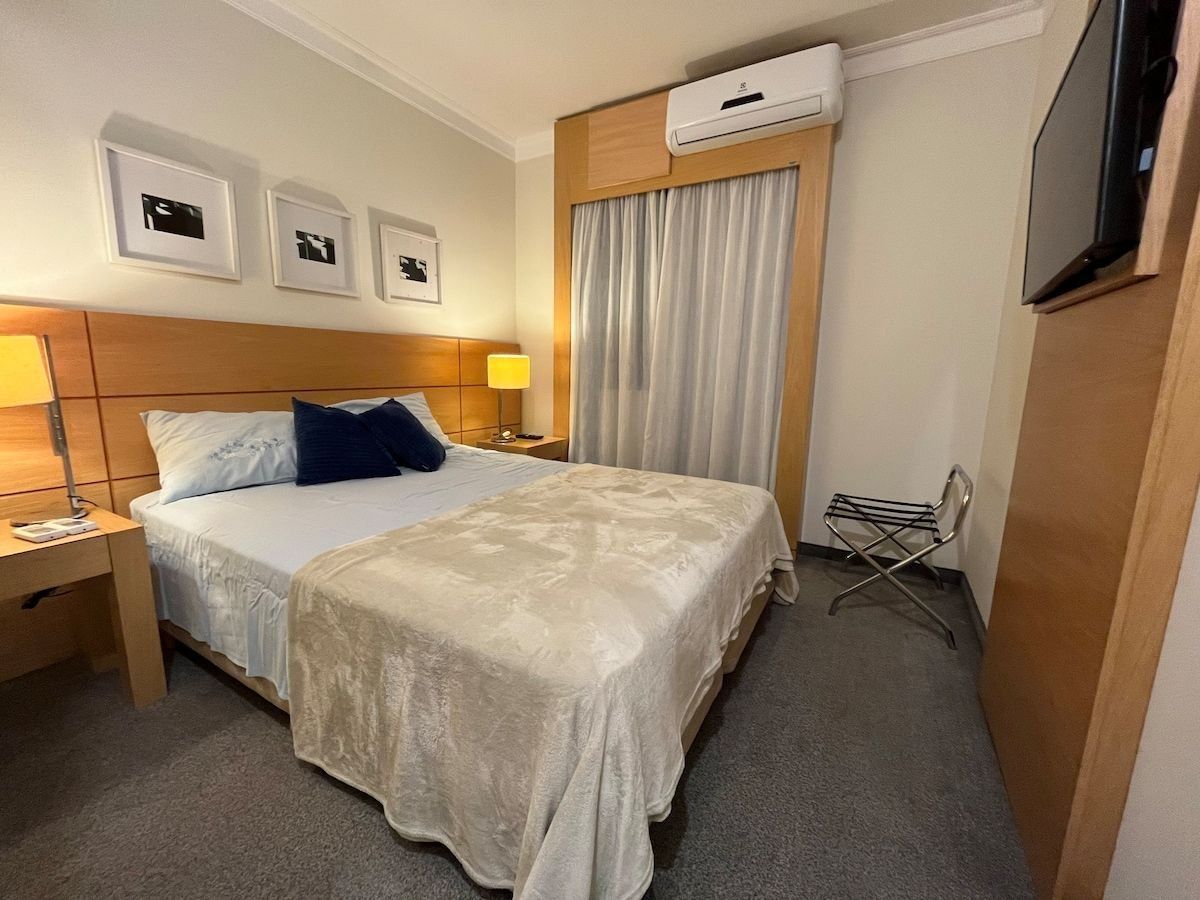A hotel room with a bed, a nightstand, a lamp, a TV, and a window with curtains.