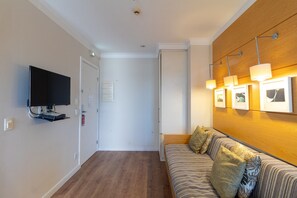 Une chambre d’hôtel dotée d’une télévision à écran plat, d’un mur en bois orné de tableaux, d’un canapé avec des coussins et d’un plancher en bois.