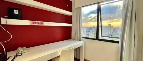 A room with a desk, a chair, a window with a city view, and a red accent wall.