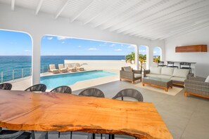 A spacious outdoor area with a pool, seating, and a view of the ocean. - Puerta Al-Mar Villa (Cole Bay)