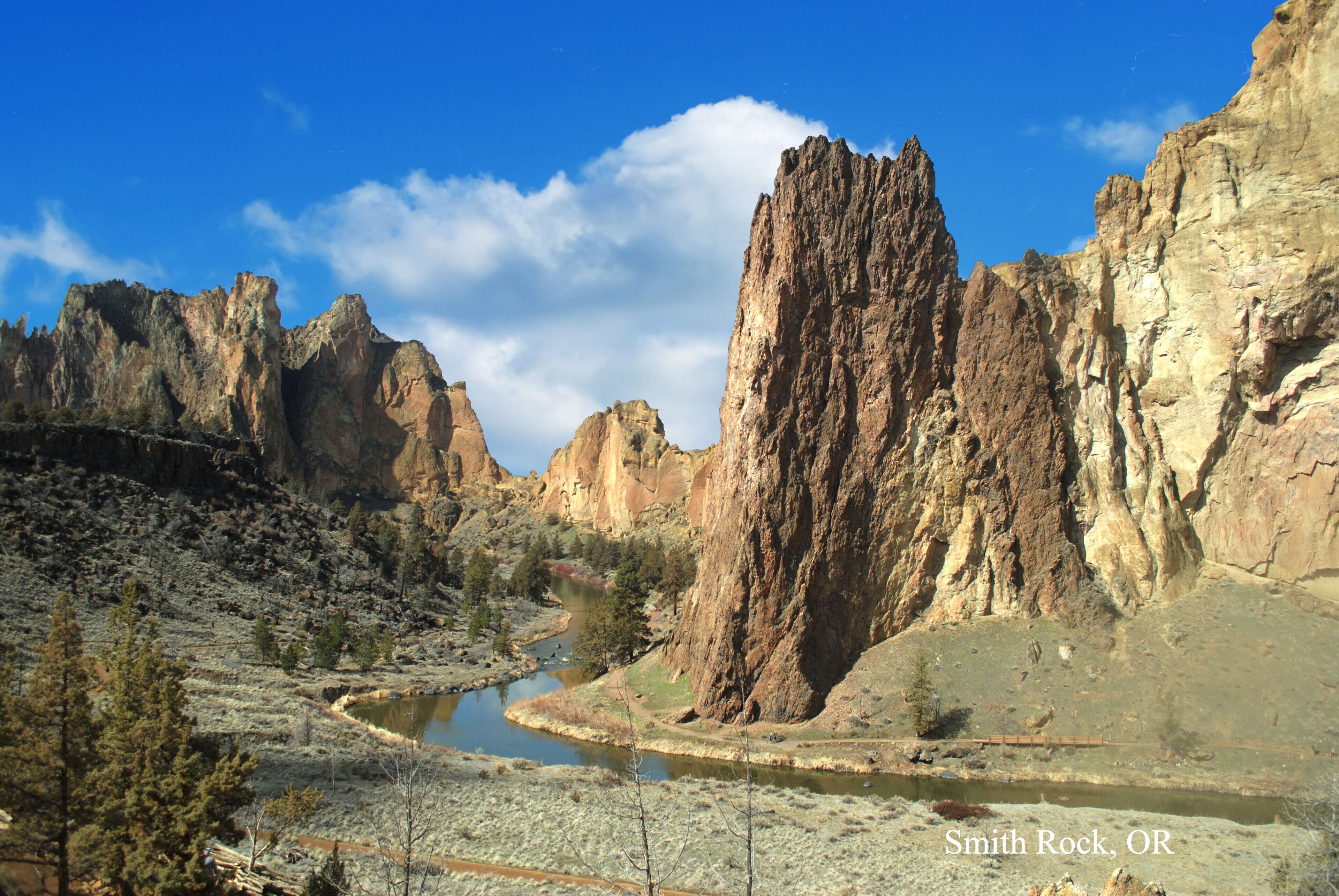 A rugged canyon landscape with a river, prominent rock formations, and sparse vegetation.