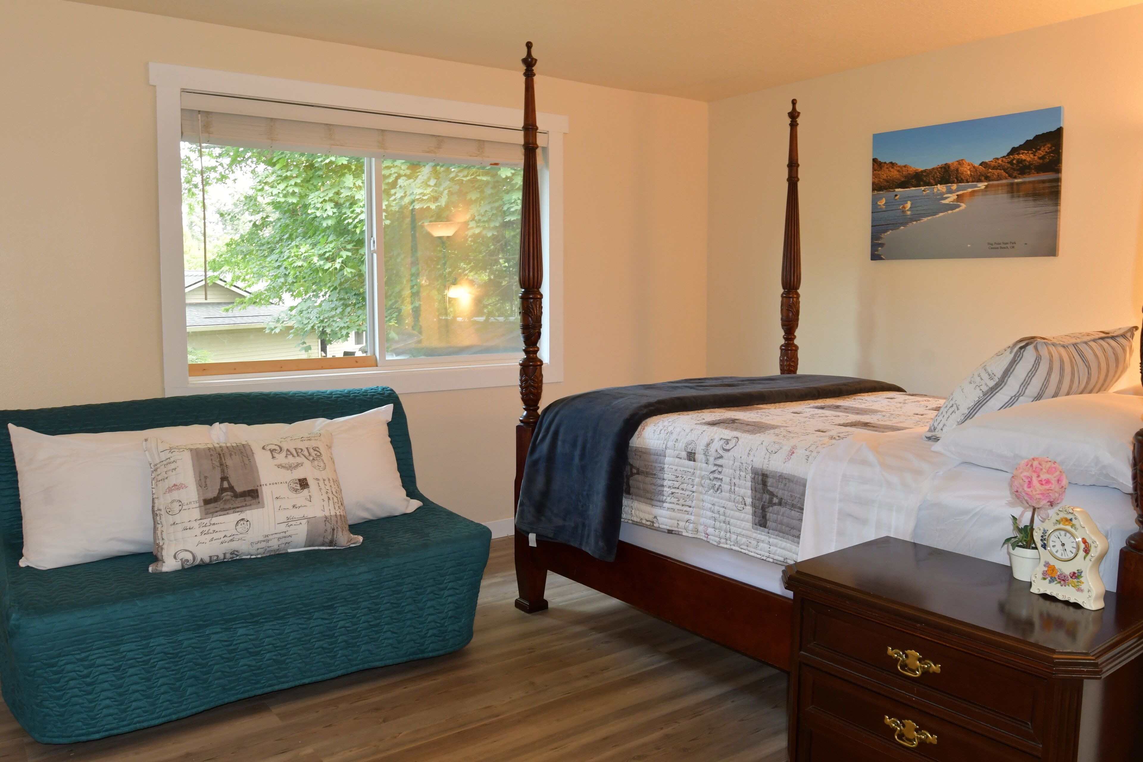A bedroom with a four-poster bed, a teal sofa, and a nightstand with a clock.
