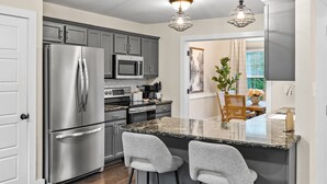 A modern kitchen with stainless steel appliances, a granite island with bar stools, and pendant lighting.