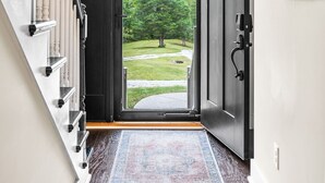 A hallway with a black door leading to a view of a grassy landscape.