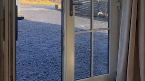 Puerta de vidrio corredera que da a un camino de grava con vistas a árboles y un edificio a lo lejos.