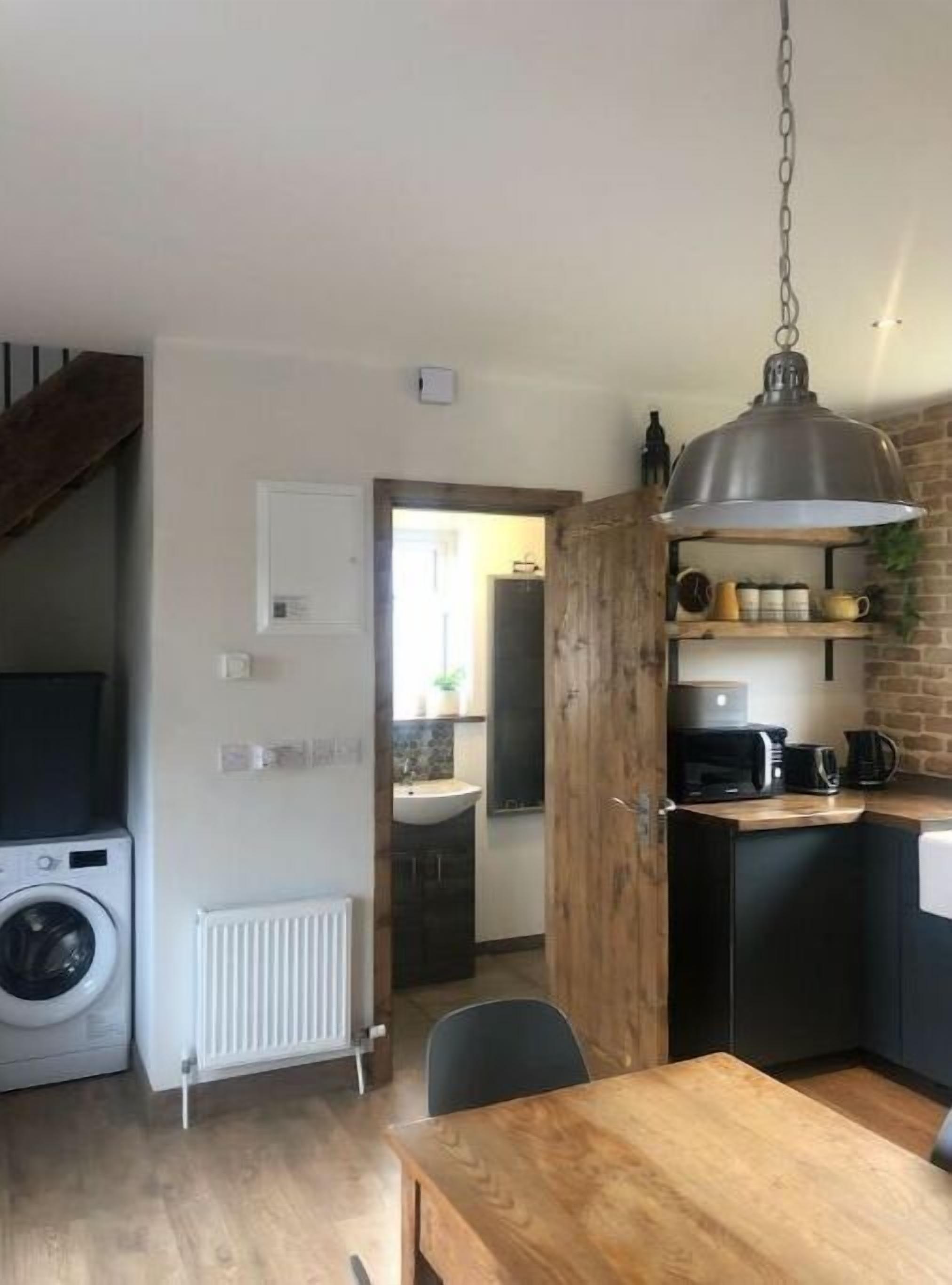 Een kleine keuken met een houten tafel, een hanglamp en een wasmachine.