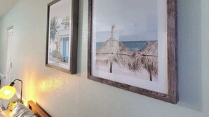 Two framed pictures on a wall, one depicting a beach scene with thatched huts and the other a building with a blue door. - NEW! Ocean Breeze! 10 Steps 2 beach! Beach view! (Clearwater)