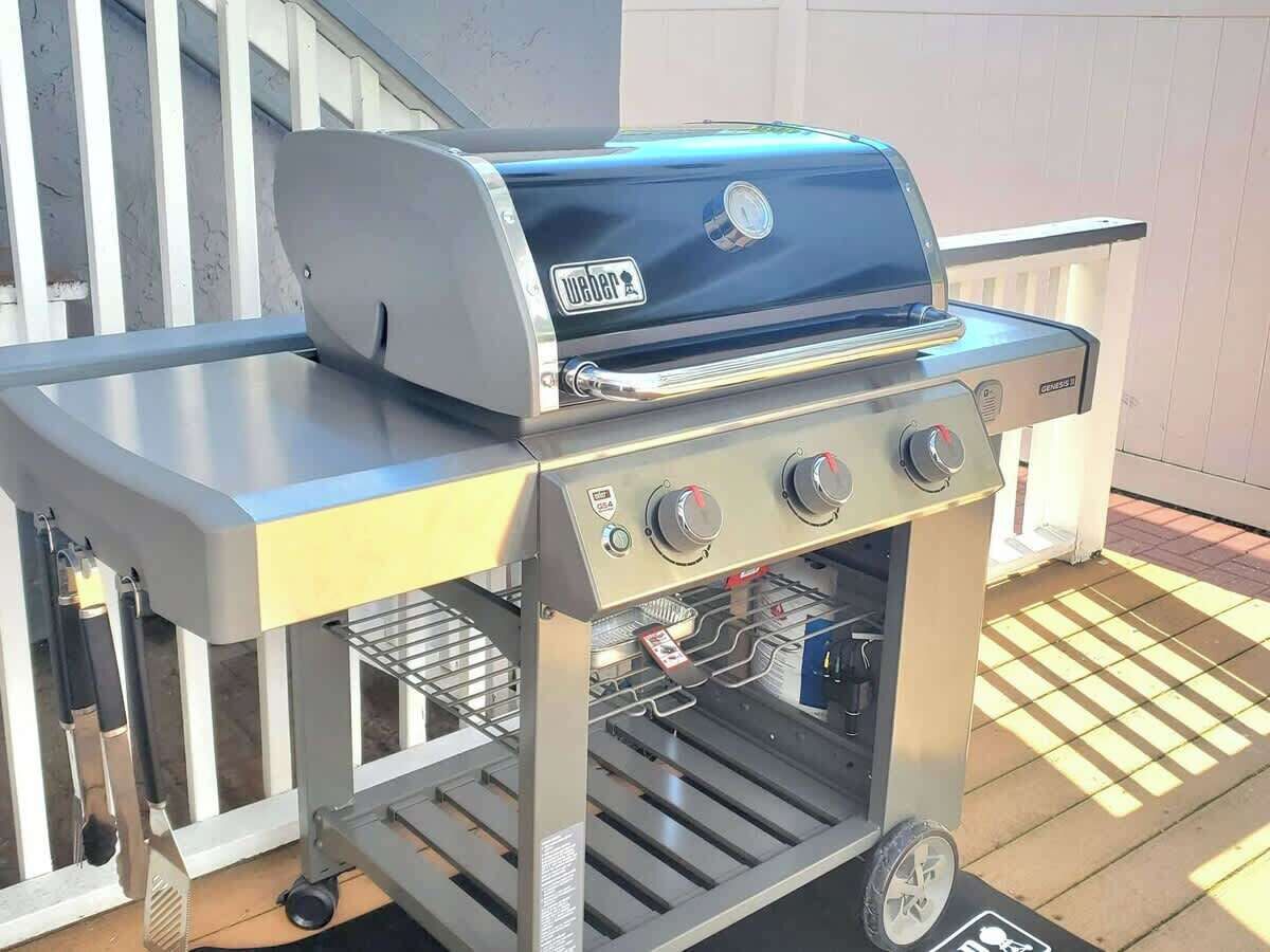 Una parrilla de gas Weber con cuatro quemadores, un estante lateral y un termómetro incorporado.