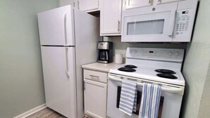 Una kitchenette compacta con refrigerador, microondas, cafetera y estufa.
