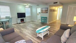 Una sala de estar con televisor, sofá, mesa de centro y un comedor con mesa y sillas.