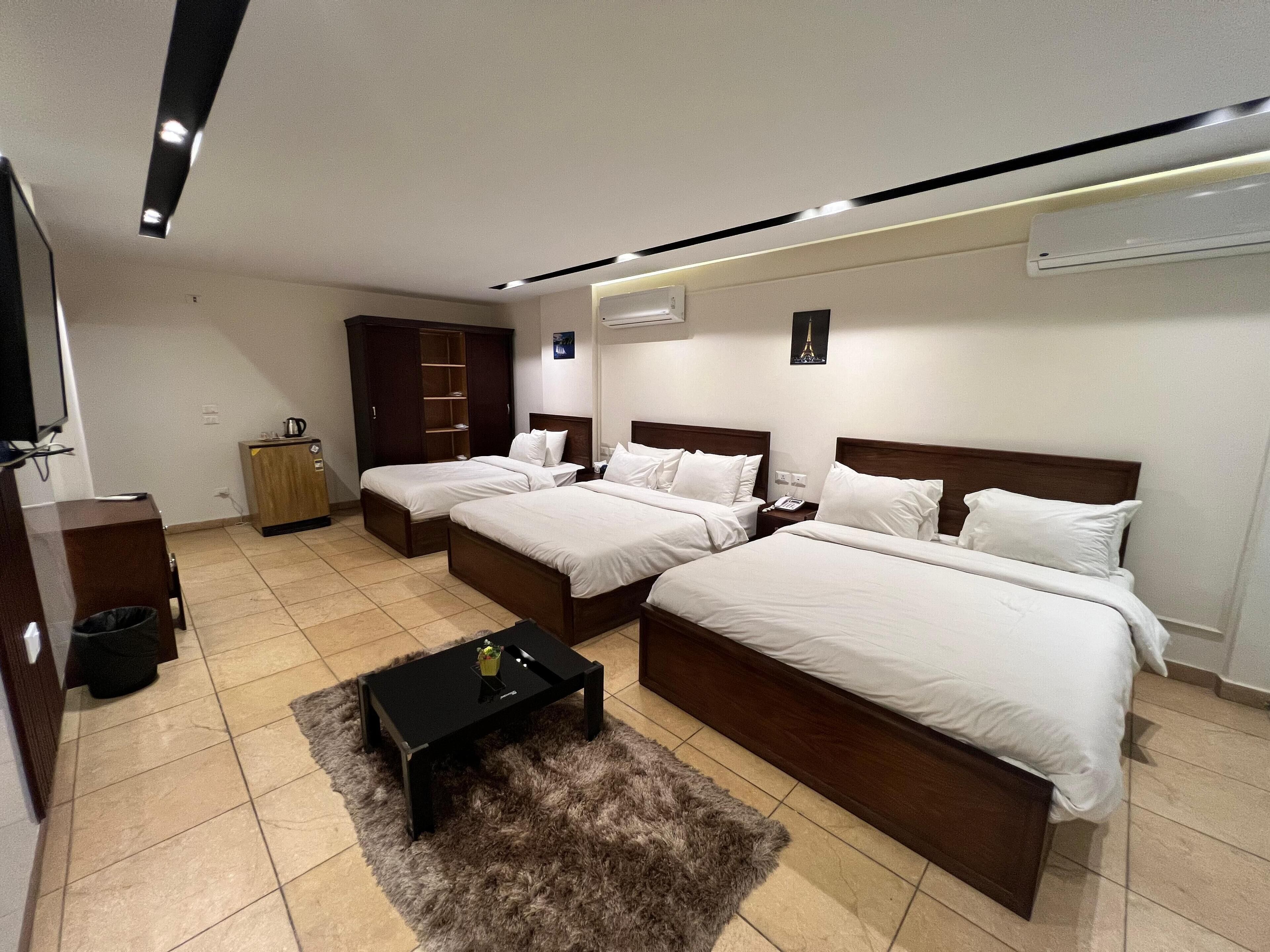 A hotel room with two beds, a small table, a wardrobe, and a TV.