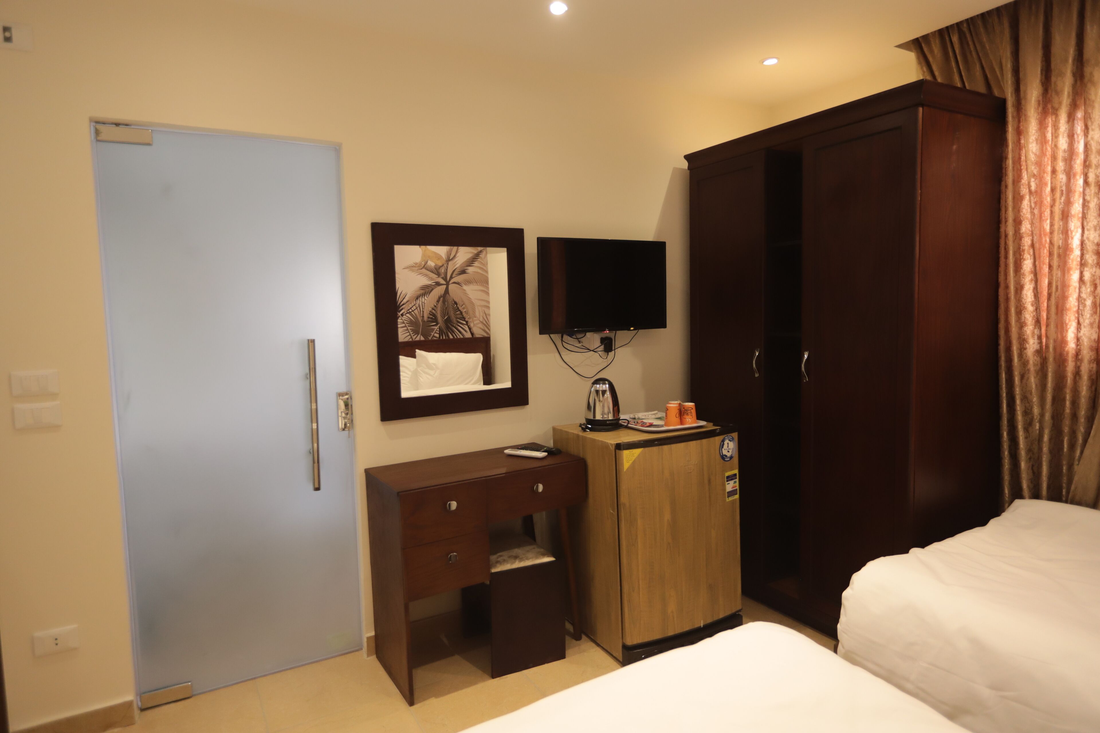 A hotel room with a bed, a desk with a chair, a wardrobe, a television mounted on the wall, and a door.