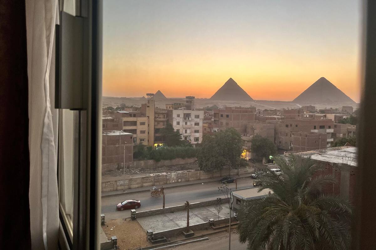 Näkymä kaupunkimaisemasta, jonka taustalla kohoavat pyramidit, ja kuvassa on myös rakennuksia sekä ajoneuvoja kulkeva katu.