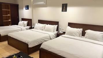 Habitación de hotel con tres camas individuales, un armario de madera, una mesita de noche con teléfono y una pequeña mesa con un florero.