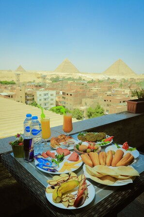 A table with food and drinks on a balcony overlooking pyramids. - King Khafren View INN (Giza)