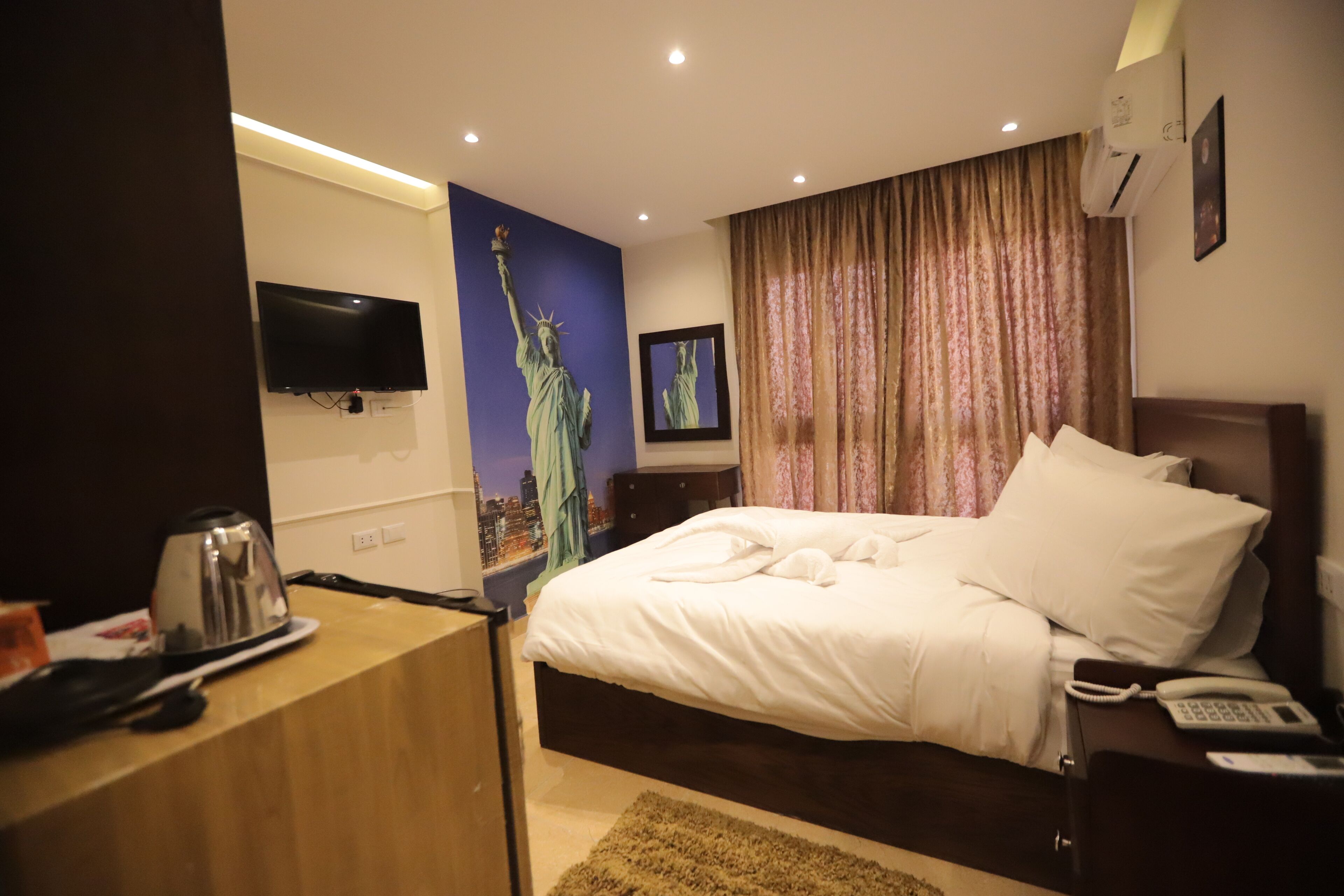 Quarto de hotel com cama, televisão de tela plana, cafeteira e telefone.