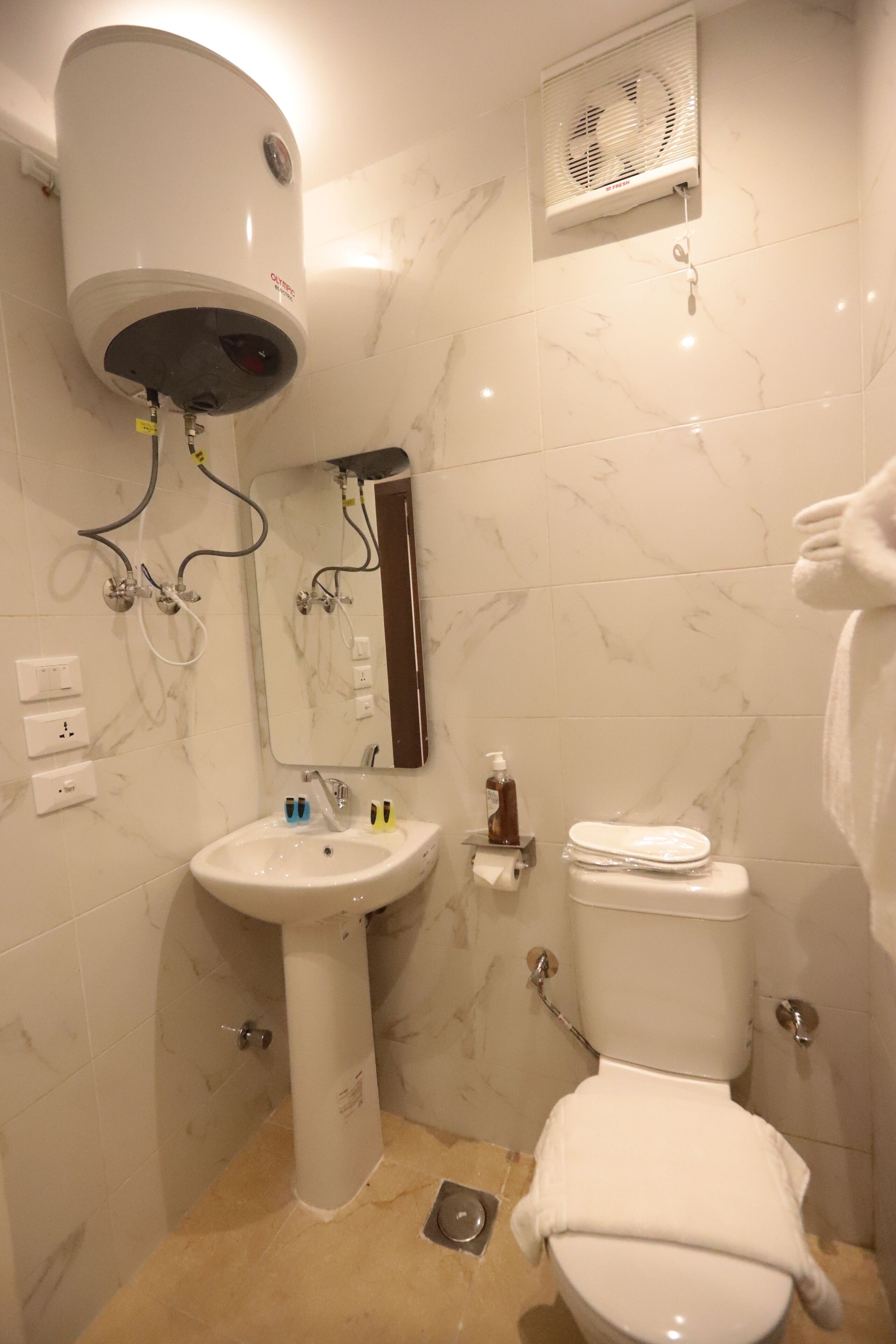 A bathroom with a white pedestal sink, a toilet, a mirror, and a wall-mounted heater.