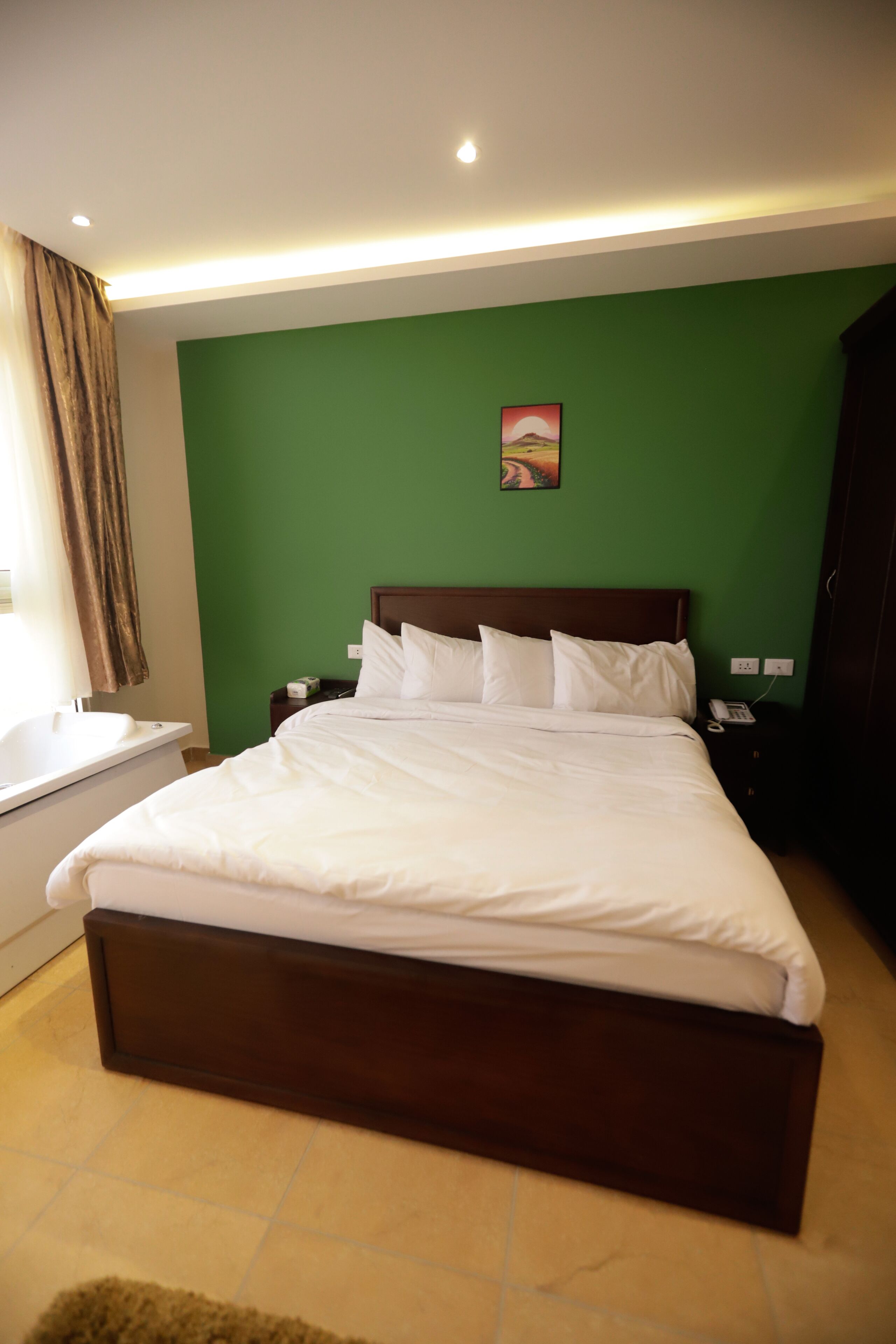 Ein ordentlich bezogenes Bett in einem Zimmer mit grünen Wänden, einem hölzernen Kopfteil und einem kleinen Nachttisch mit einem Telefon.
