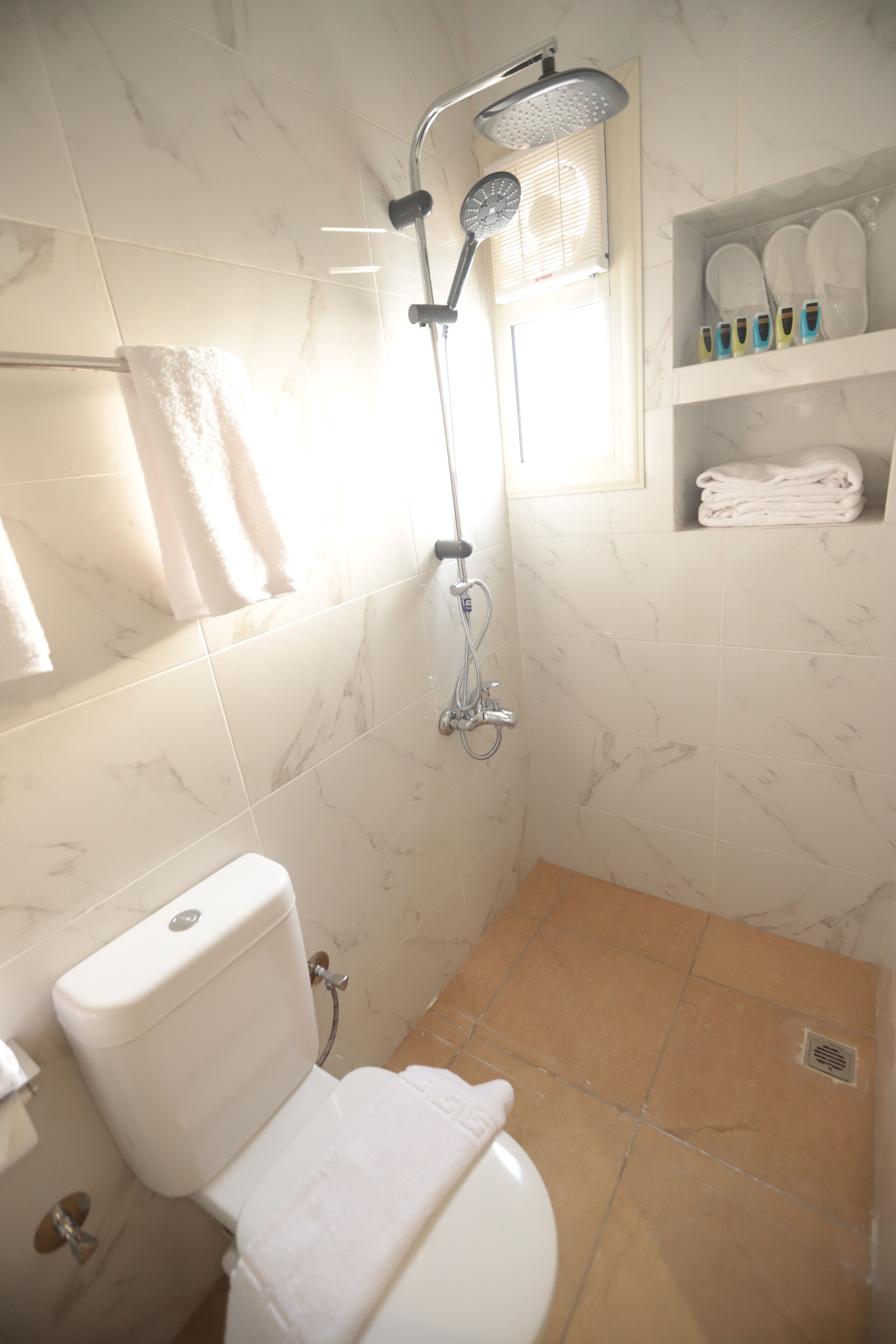 A bathroom with a toilet, shower, and a shelf with folded towels.