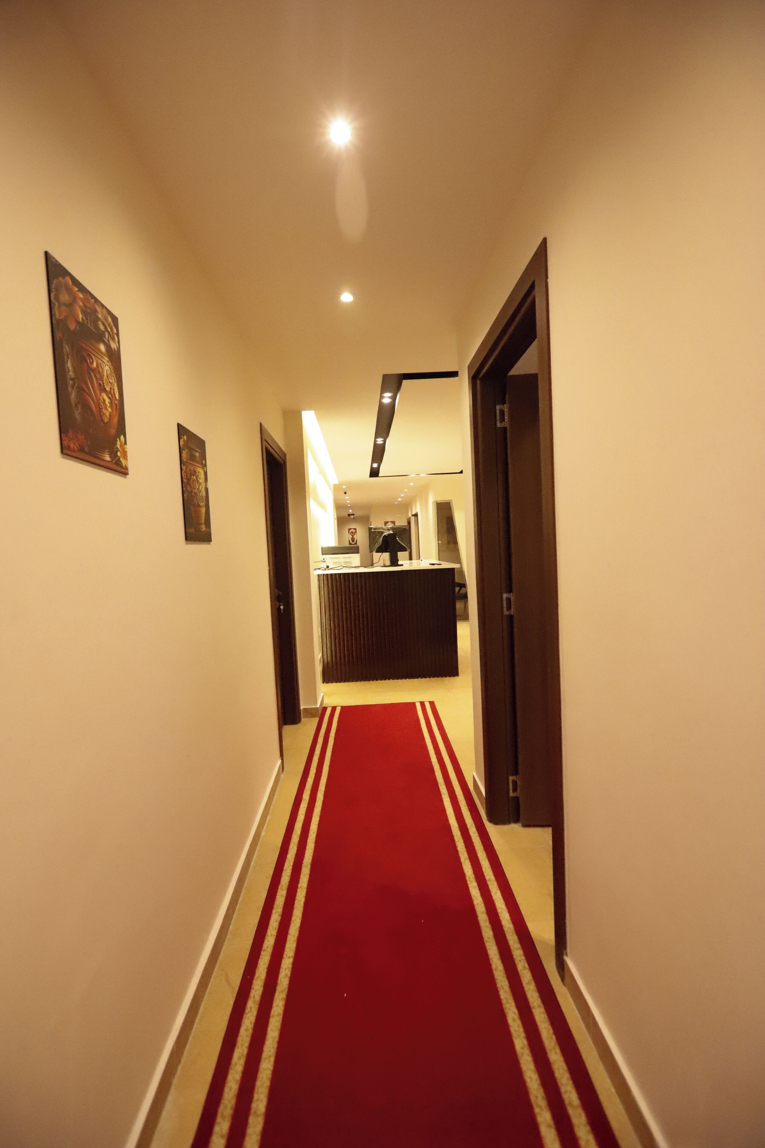 A hotel hallway with a red carpet, a reception desk, and framed artwork on the walls.