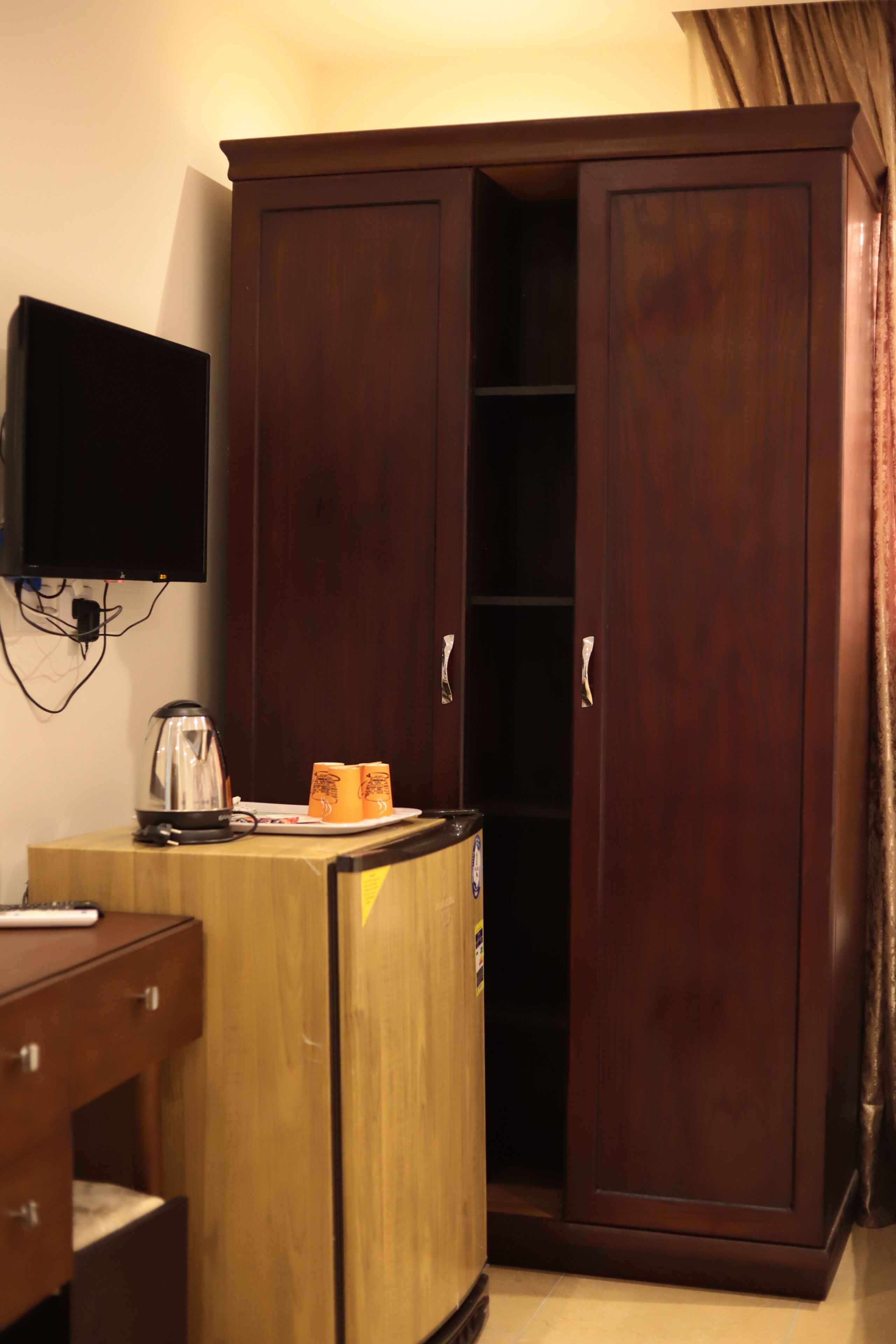 Ein Zimmer mit Holzschrank, einem kleinen Tisch mit Wasserkocher und einem flachbildfernseher an der Wand.