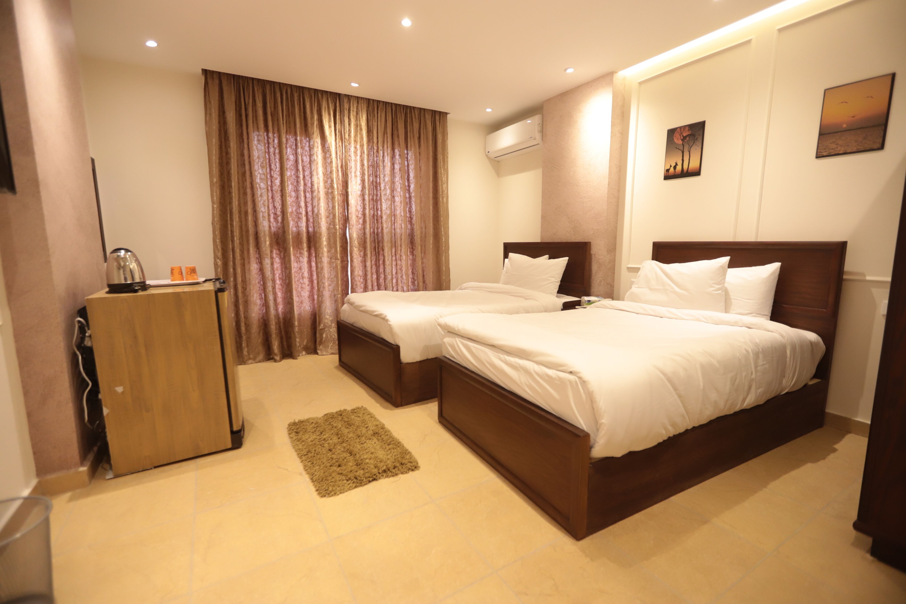 Een hotelkamer met twee bedden, een houten garderobe, een klein vloerkleed en een schilderij aan de muur.