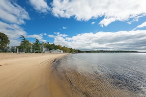A beach with a sandy shore, a calm body of water, and a clear sky with clouds.