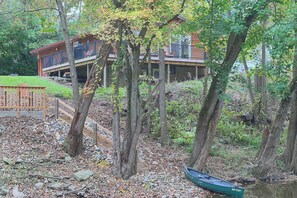 A cabin with a deck overlooking a body of water, surrounded by trees and a wooden fence.