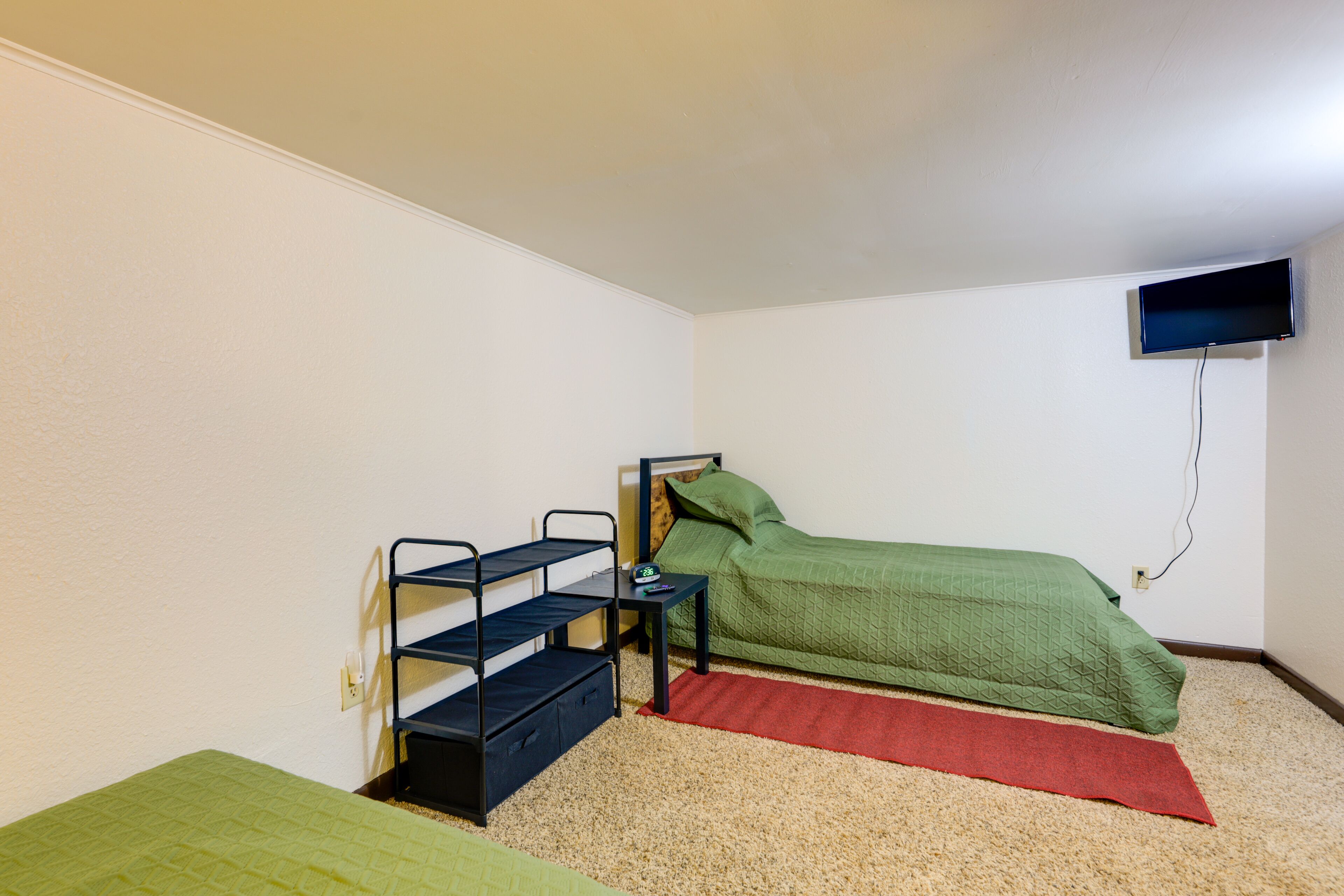 A small, sparsely furnished room with a bunk bed, a desk with a chair, a television mounted on the wall, and a carpeted floor.