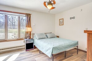 A bedroom with a bed, a nightstand, a lamp, a window with curtains, and a ceiling fan. - Riverfront Covington Cabin w/ Deck & Fire Pit! (Covington)