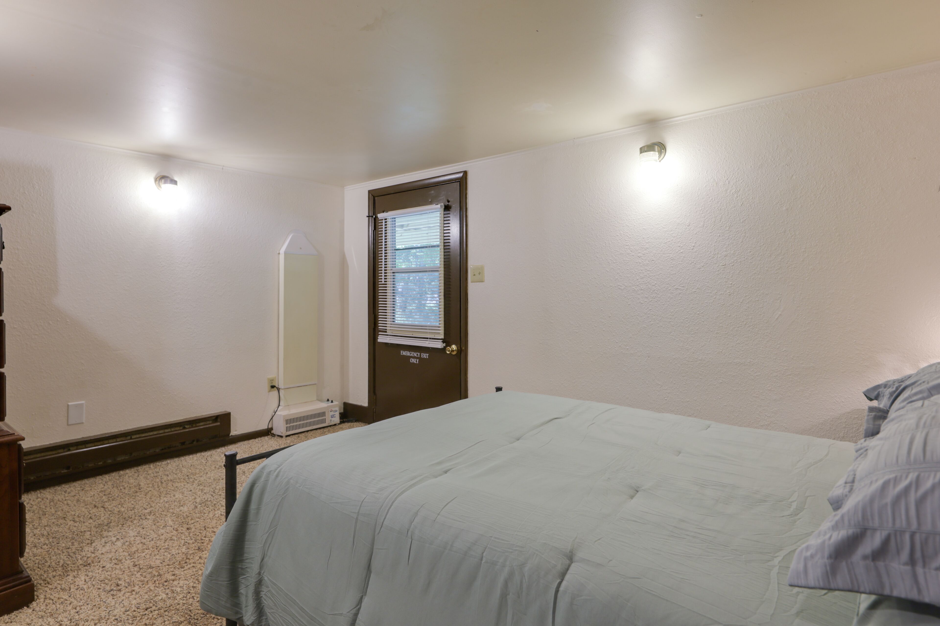 Quarto com cama, penteadeira, espelho e porta com janela.