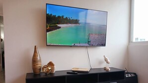 A flat-screen TV mounted on a wall above a black entertainment unit with a remote control, a decorative bird, and two vases. - Cozy Elegance : Tu Rincón en San Juan (San Juan)